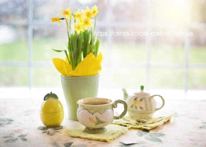 Daffodils in a green pot beside a teacup, teapot, and lemon-shaped jar