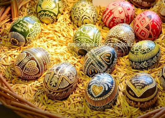 Basket of dark green, brown and black pysanky eggs with white ornament, nestled in straw