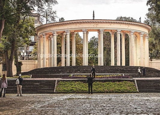 Circular colonnade on a stone terrace above the Dnipro riverside promenade, with visitors and autumn trees.