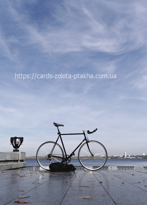 Black road bike parked on the Dnipro riverfront with the city skyline across the water