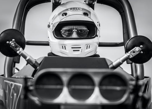 Schwarzweißaufnahme eines Dragster-Fahrers mit Helm und Sonnenbrille hinter dem Steuer