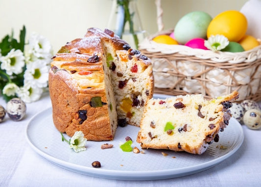 Sliced Easter bread with dried fruit beside a basket of colored and quail eggs