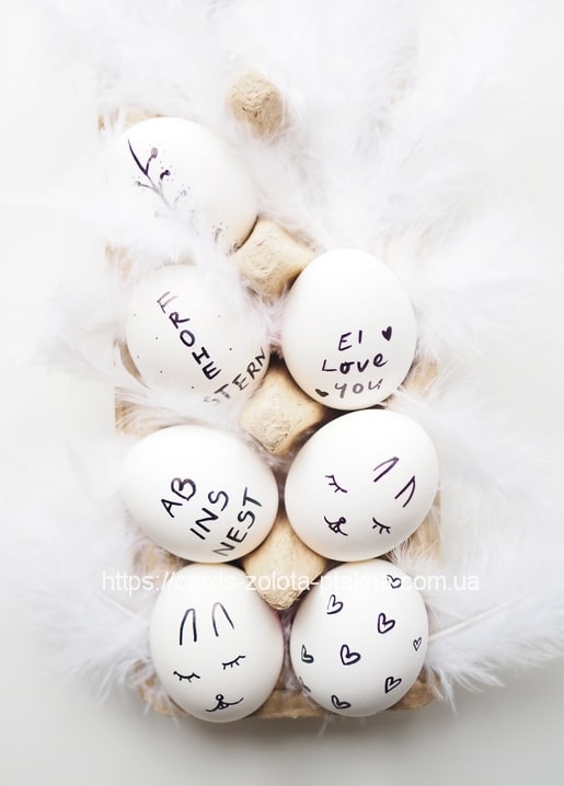 White eggs doodled with bunny ears, hearts, and sleepy faces in black marker among white feathers