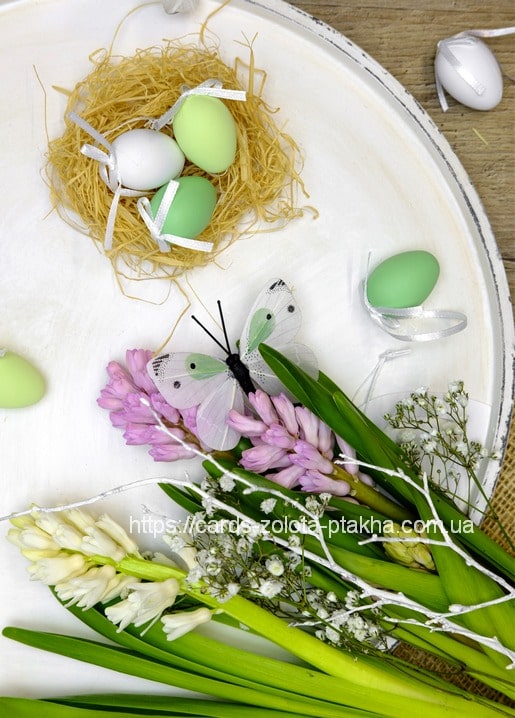 Straw nest with speckled eggs, a butterfly, and pink hyacinths on a white tray