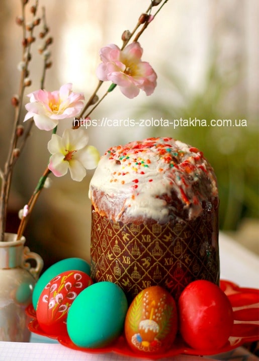 Frosted Easter paska cake beside painted eggs, pussy willow, and cherry blossom branches