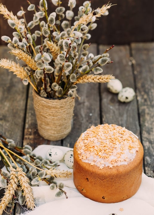 Golden Easter paska loaf beside pussy willow branches and speckled quail eggs on a wooden table