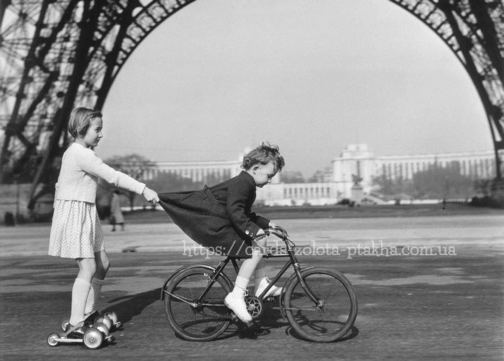Black-and-white postcard of two girls racing by the Eiffel Tower — one on roller skates, one on a bicycle