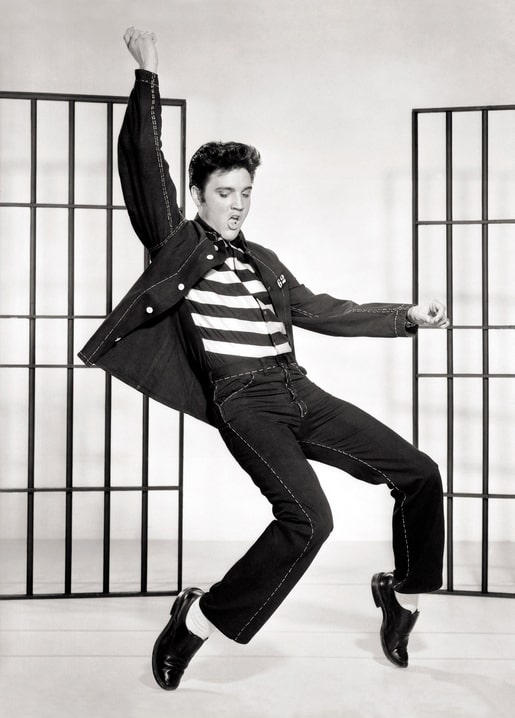 Elvis Presley in einer Tanzbewegung mit Jeansjacke vor Gefängnisgittern