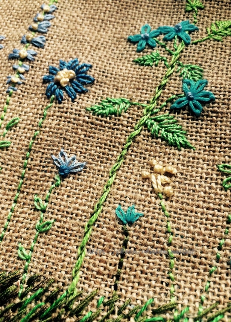 Handbestickte blaue und türkisfarbene Wildblumen mit Knötchenstich auf Jute