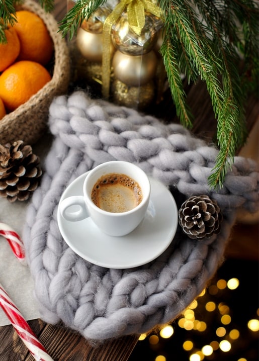 Espresso cup on a chunky knit blanket with oranges, pinecones and a candy cane