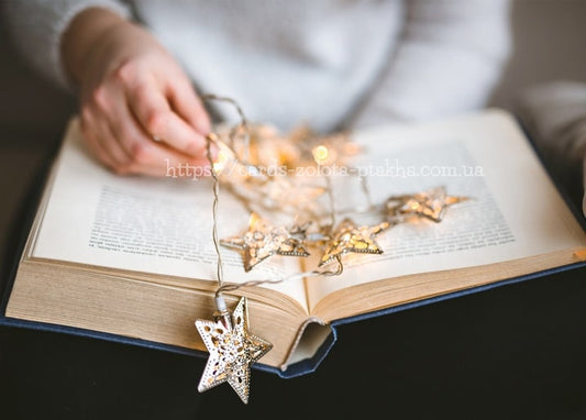 Hand entwirrt eine Lichterkette mit Silbersternen auf einem aufgeschlagenen Buch