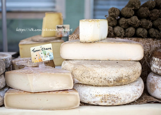 Wheels of aged cheese at a farmers market stall with a Tomme Chèvre label and hay bales