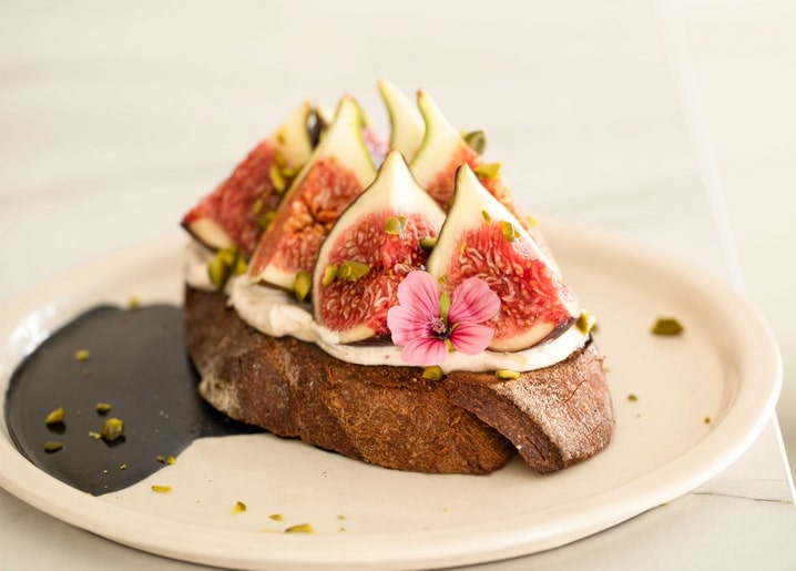 Toast mit Feigenscheiben, Frischkäse, Pistazien und essbarer Blüte, mit Balsamico beträufelt
