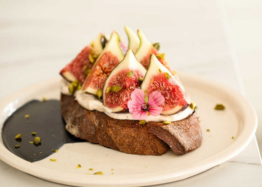 Toast mit Feigenscheiben, Frischkäse, Pistazien und essbarer Blüte, mit Balsamico beträufelt