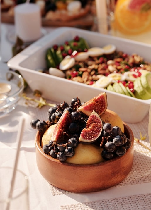 Дерев'яна миска з інжиром, виноградом і грушами на сонячному столі, позаду салатниця
