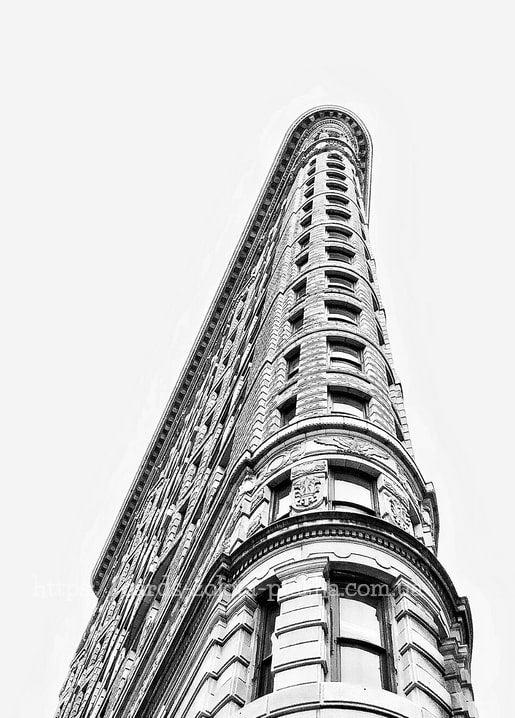 Low-angle black-and-white photo of the Flatiron Building's triangular facade against a bright sky