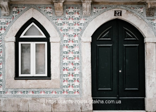 Weiße Fassade mit rosa Blumenkacheln, spitzbogigem Fenster und schwarzer Flügeltür Nr. 27.