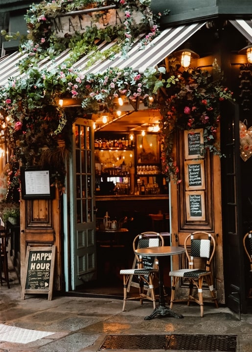 Фасад кафе, вкритий трояндами й гірляндами, з табличкою «Happy Hour» біля входу