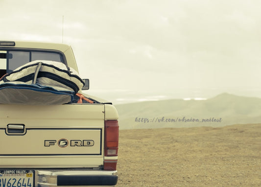Ladefläche eines alten Ford-Pickups mit Surfboard vor Wüstenbergen