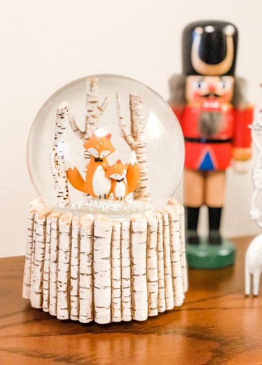 Schneekugel mit Fuchsfamilie zwischen Birken, im Hintergrund unscharf ein Nussknacker.