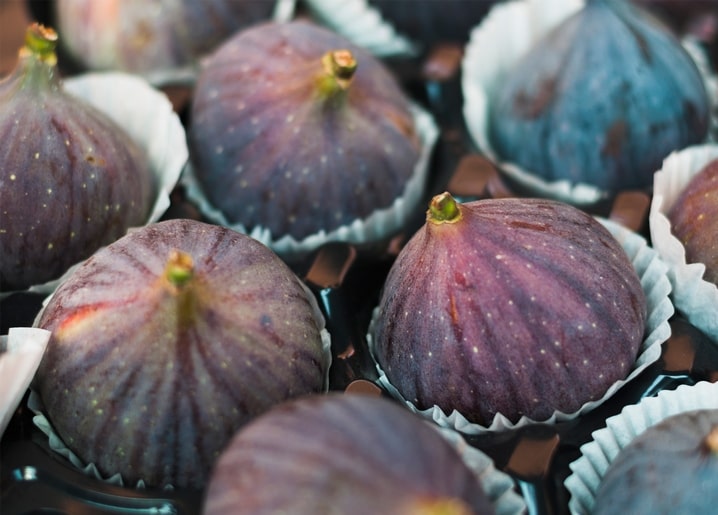 Close-up of fresh purple figs with green stems nestled in white paper cups