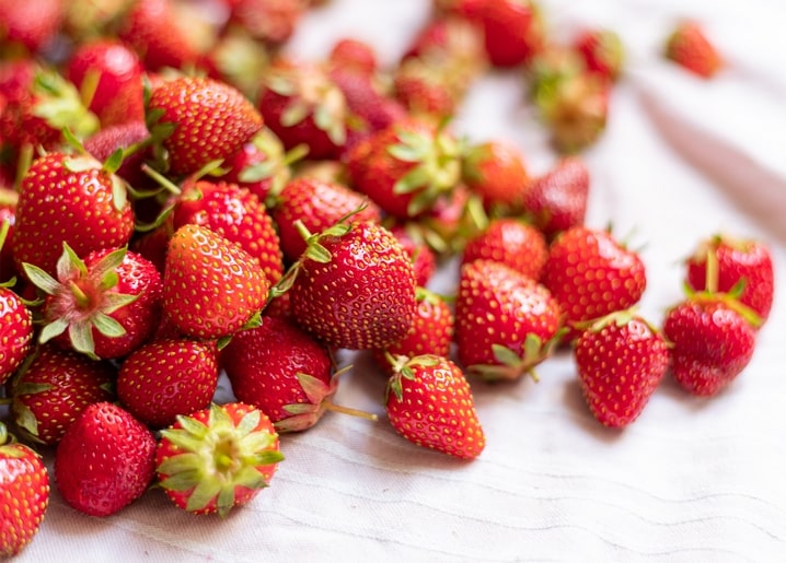 Haufen frischer Erdbeeren mit grünen Kelchblättern auf weißem Leinen