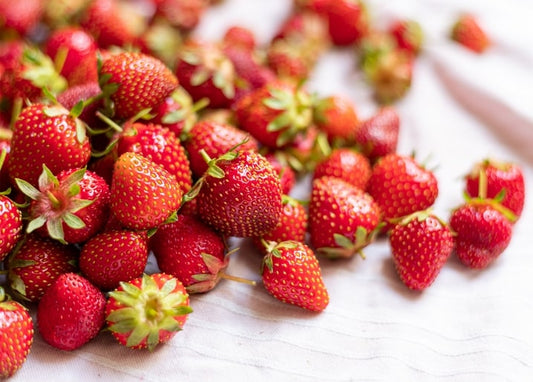 Haufen frischer Erdbeeren mit grünen Kelchblättern auf weißem Leinen