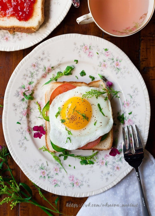 Toast mit Spiegelei und Tomate auf geblümtem Teller neben einer Tasse Tee