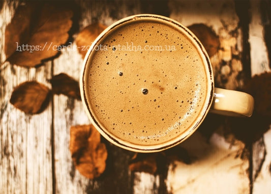 Overhead view of a frothy coffee cup on a wooden table scattered with dried autumn leaves