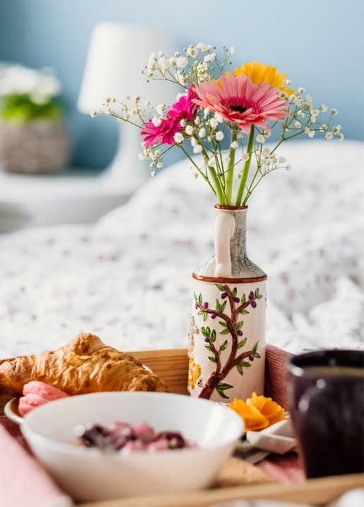 Hand-painted ceramic vase with gerberas and baby's breath beside a croissant on a breakfast tray