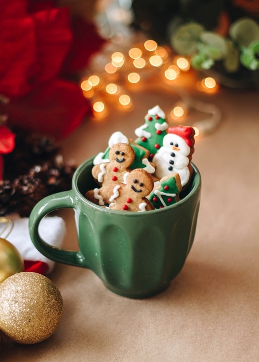 Green mug filled with iced gingerbread man, tree and snowman cookies by Christmas lights