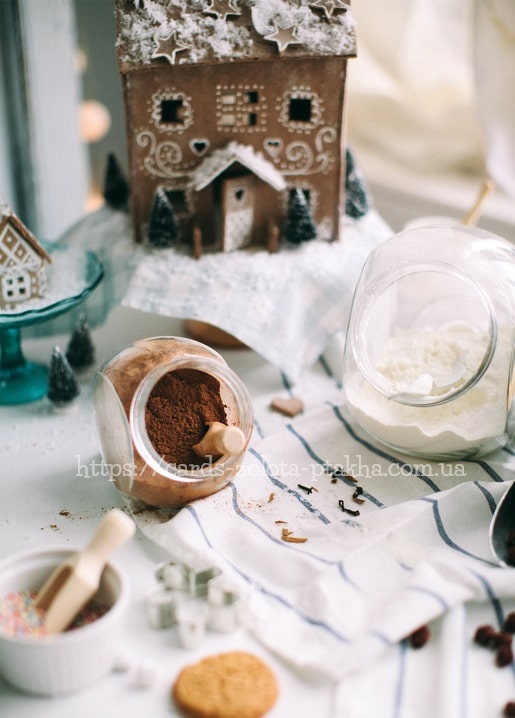 Lebkuchenhaus zwischen Gläsern mit Zimt, Puderzucker und Ausstechformen