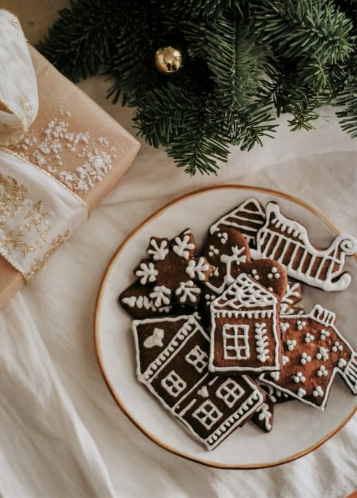 Plate of iced gingerbread houses, snowflakes and a sleigh cookie beside a wrapped gift and pine branch