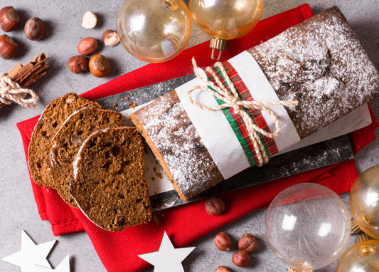 Aufgeschnittenes Lebkuchenbrot mit Puderzucker und Karoband zwischen Haselnüssen und Glaskugeln