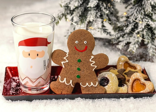 Gingerbread man cookie beside a Santa-print glass of milk and jam-filled cookies on snow