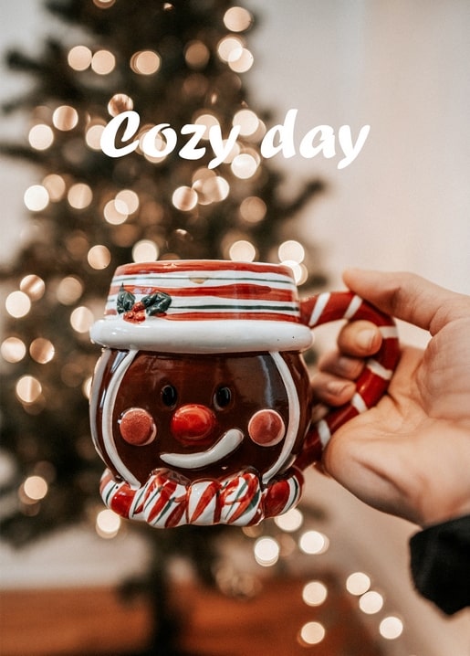 Hand hält eine Tasse in Form eines Lebkuchenmanns vor unscharfen Weihnachtsbaum-Lichtern
