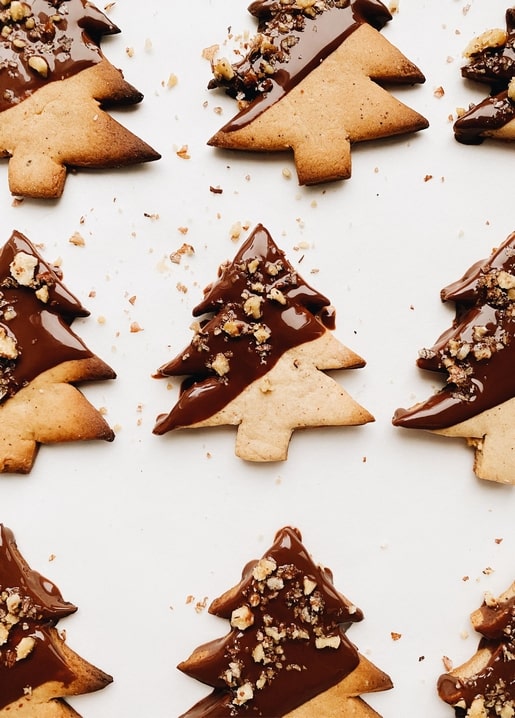 Lebkuchen-Tannenbäume mit Schokoladenglasur und gehackten Nüssen, reihenweise angeordnet.