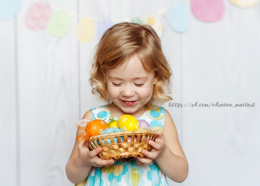 Smiling girl holding a basket of colorful Easter eggs with a pastel garland background