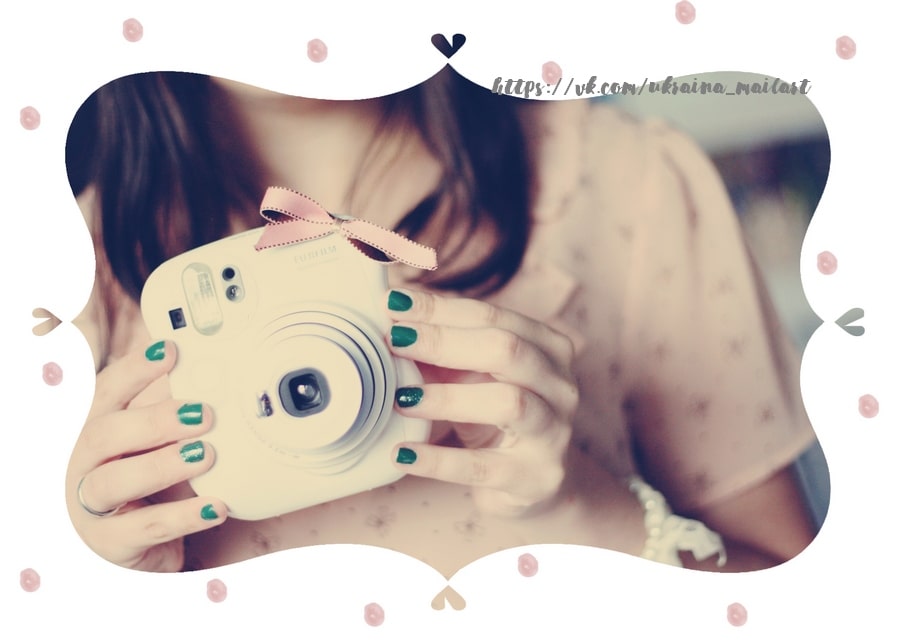 Girl with green nail polish holding a white Fujifilm Instax camera tied with a pink ribbon