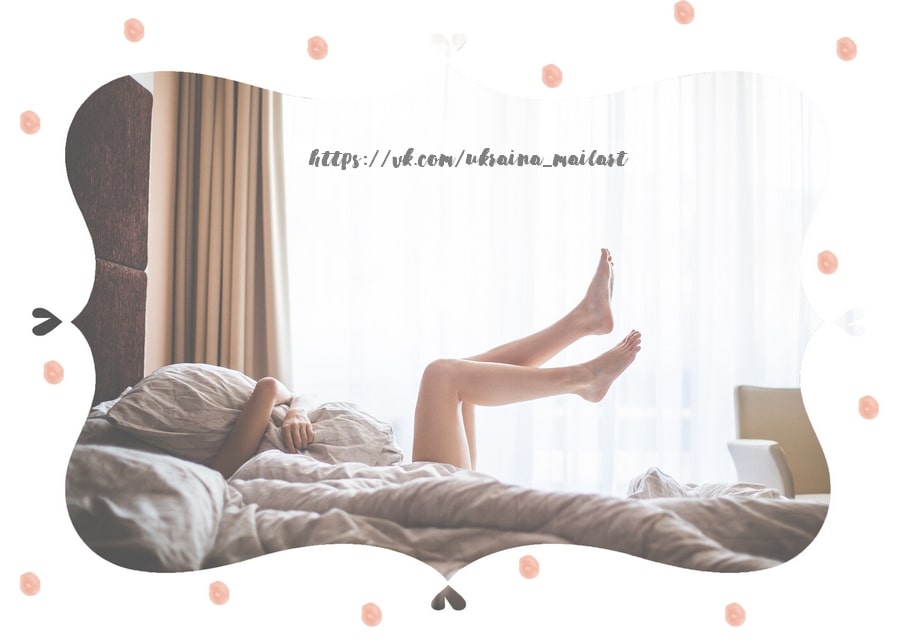 Young woman lying in bed with legs raised against a sunlit curtained window