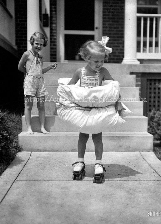 Schwarz-weißes Vintage-Foto: Mädchen auf Rollschuhen umarmt ein Kissen, ein weiteres Mädchen lacht auf der Veranda