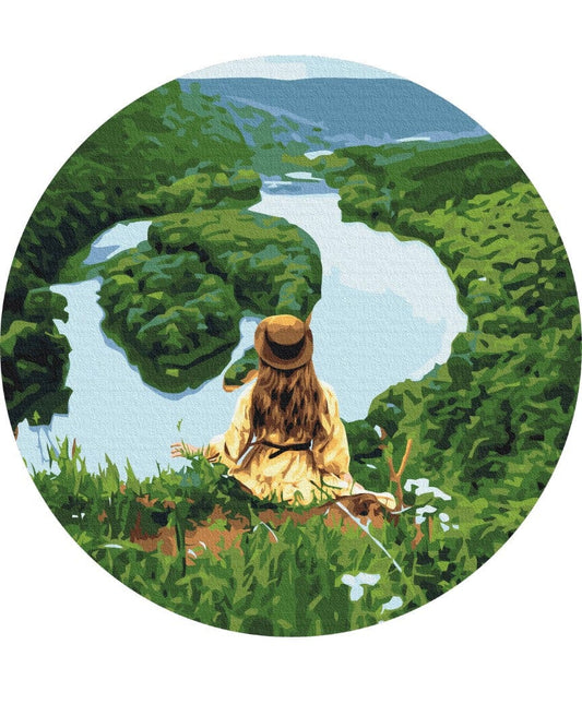 Girl in a yellow dress and hat looking out over a winding river between green hills