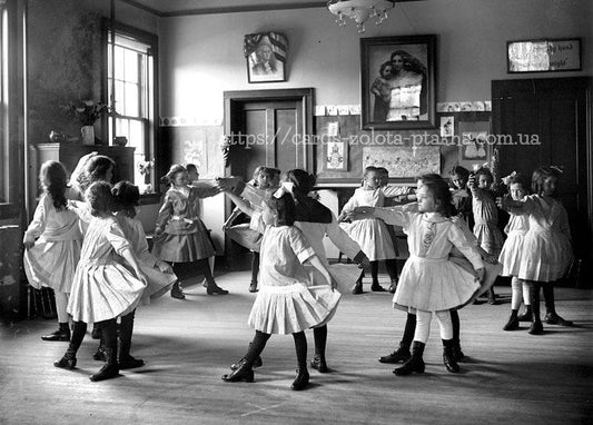 Vintage-Foto von Schulmädchen in weißen Schürzen, die im Kreis im Klassenzimmer tanzen