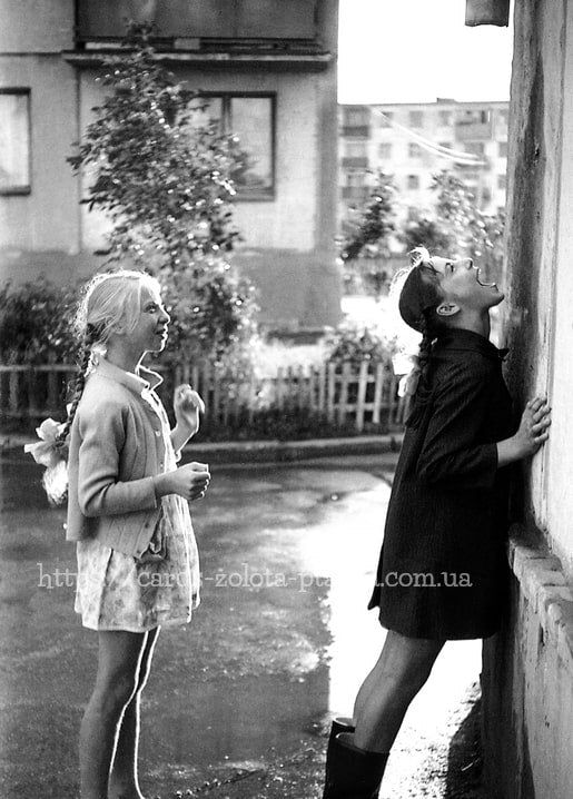 Schwarzweißfoto zweier Mädchen im Hof, eine fängt Regentropfen mit der Zunge auf