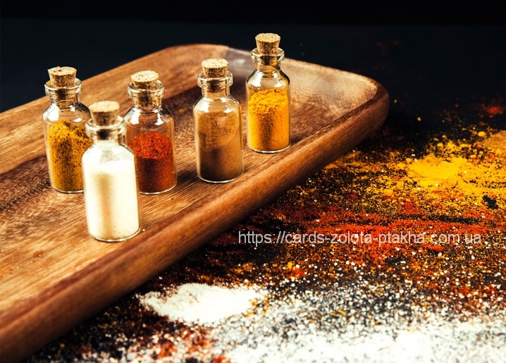 Five small cork-stoppered glass bottles of colorful ground spices on a wooden board