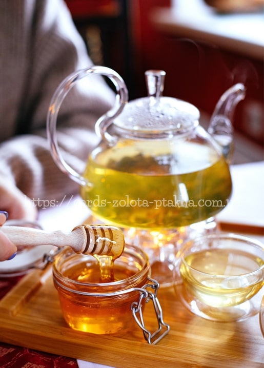 Glass teapot brewing tea beside honey drizzling from a wooden dipper