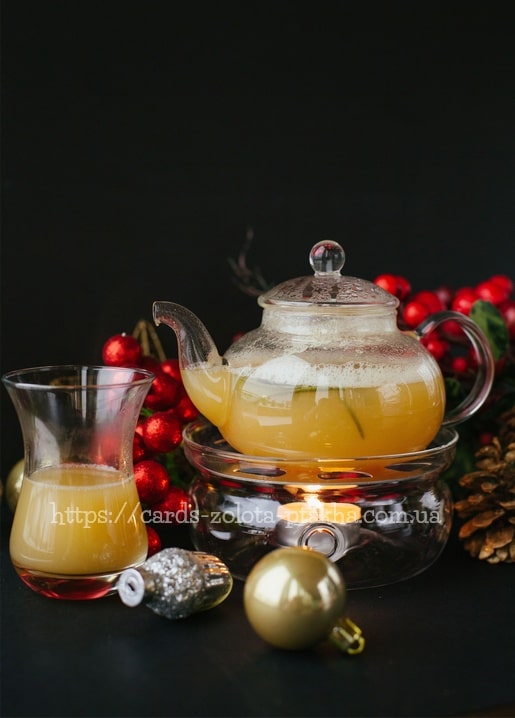 Glas-Teekanne mit heißem Punsch neben roten Weihnachtskugeln und Beeren