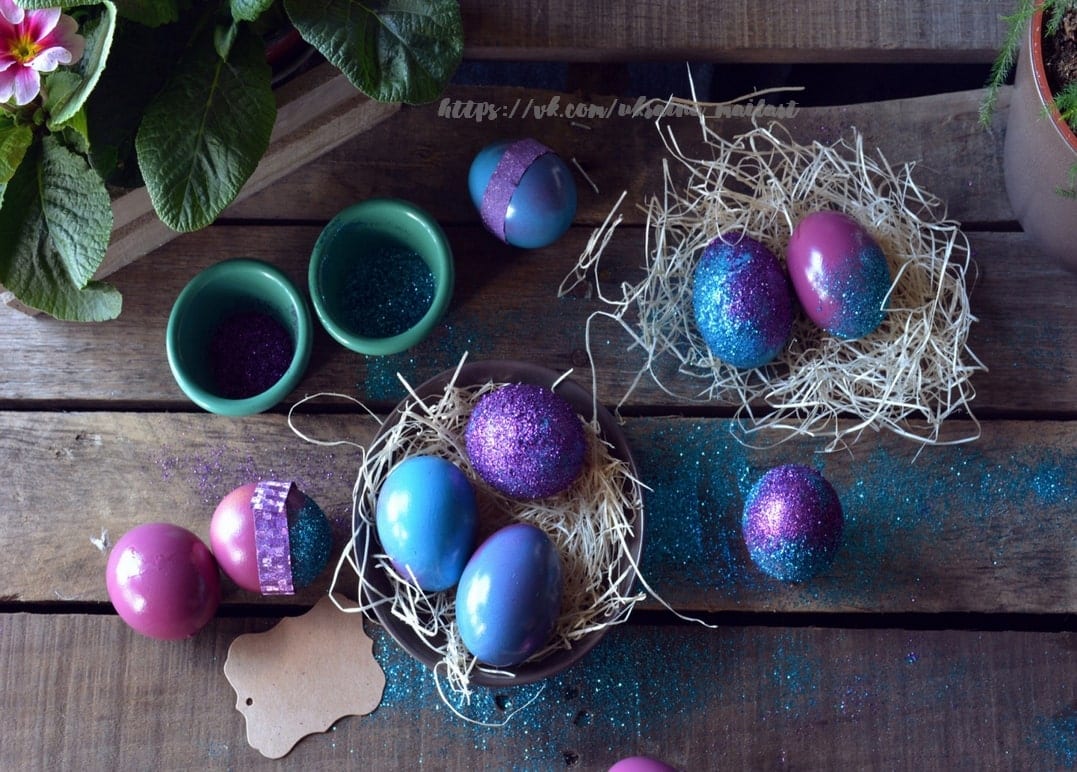 Blaue, violette und rosa Glitzereier in strohgefüllten Nestern