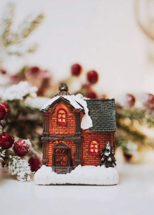 Kleines leuchtendes Weihnachtshaus mit Schnee auf dem Dach, Tannenzweigen und roten Beeren