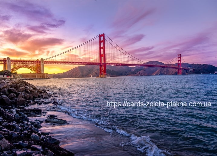 Golden Gate Bridge leuchtet rot bei Sonnenuntergang über einer felsigen Pazifikküste.